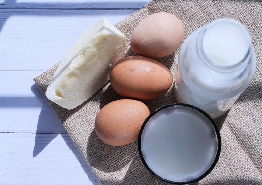 Overhead view of eggs, milk, and cheese on burlap, highlighting rustic food essentials.